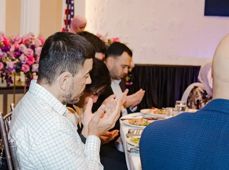 Guests applauding at their table during the program, floral arrangements along the wall behind them