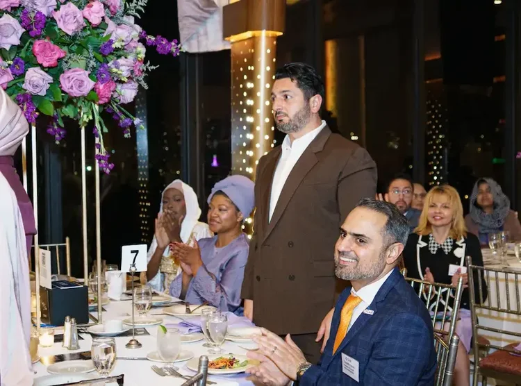 Guests at a round table applauding during the program, tall lilac centerpieces above them