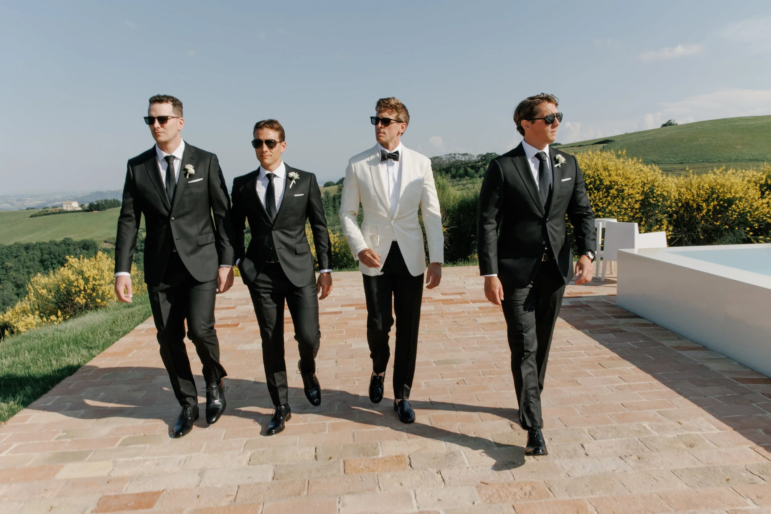 Groom in a white dinner jacket with groomsmen in custom black suits by Atelier Suiting