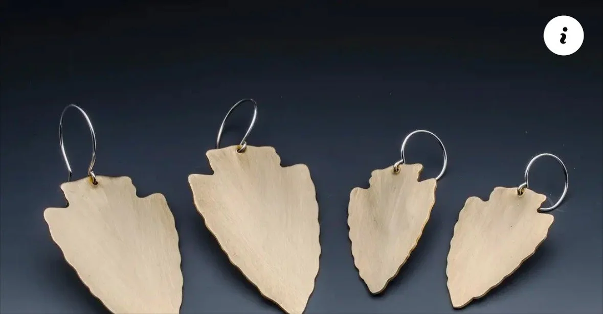 Four handmade arrowhead earrings with silver ear wires on a dark background
