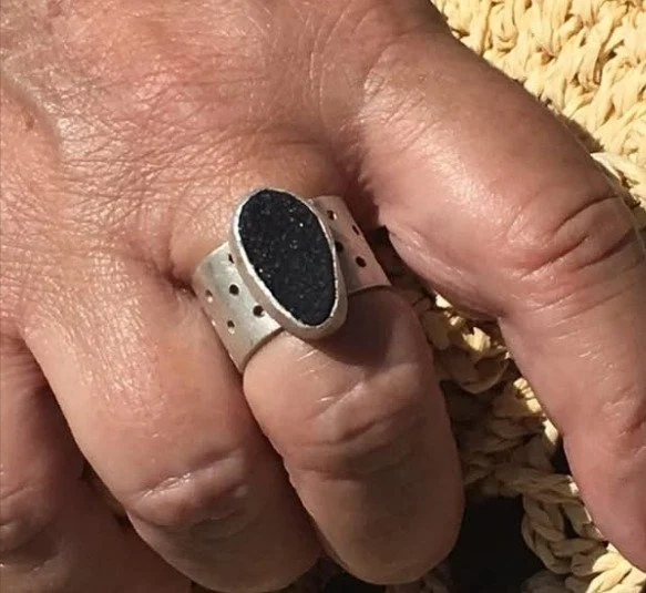 Hand wearing a handmade sterling silver ring with a dark druzy stone and perforated band