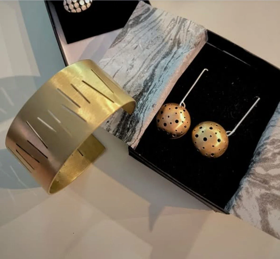 Handmade brushed brass cuff with cutout lines and dome earrings with perforated dots in a black gift box