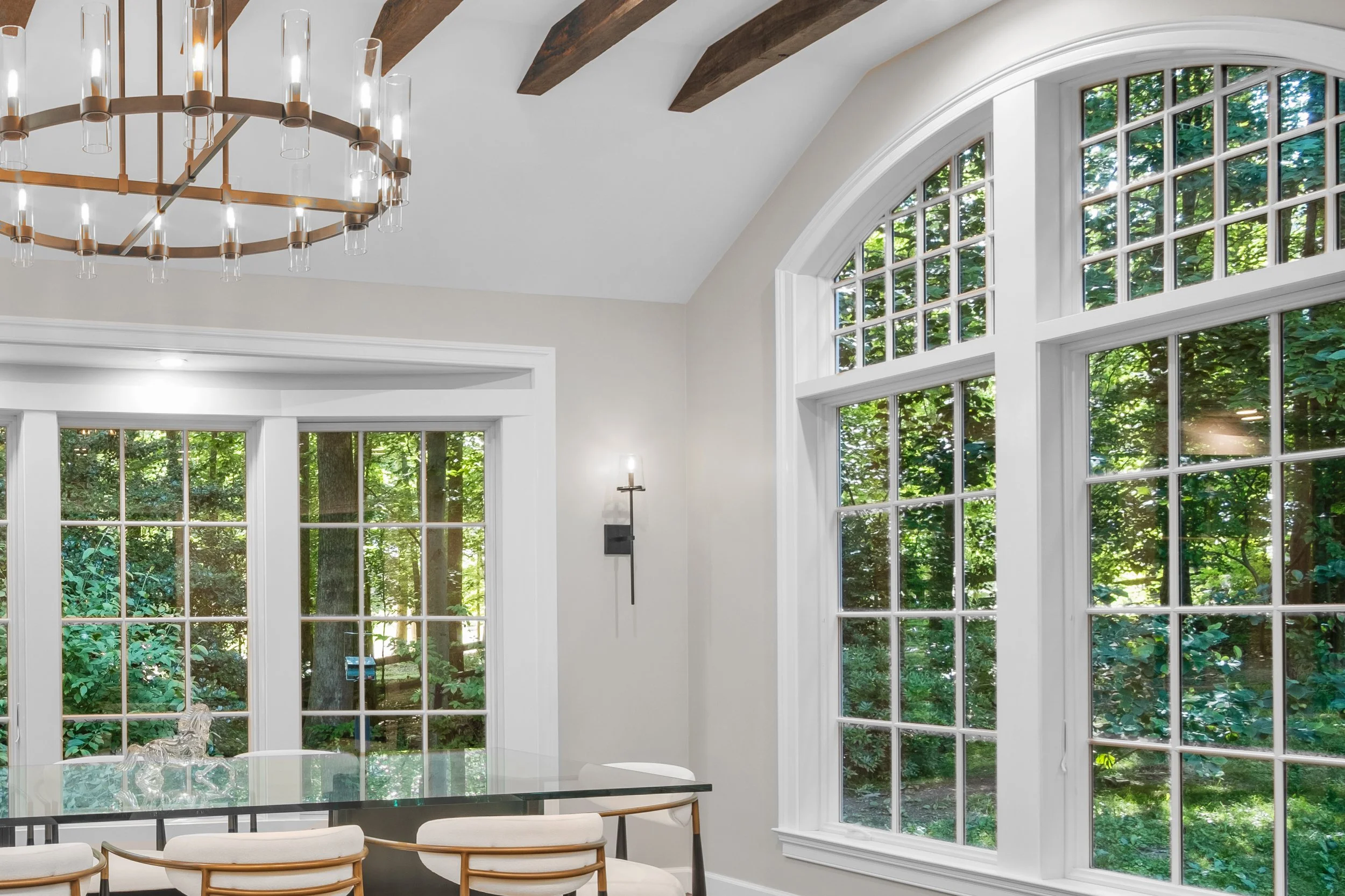Dining area with tall arched windows, ceiling beams and a chandelier.