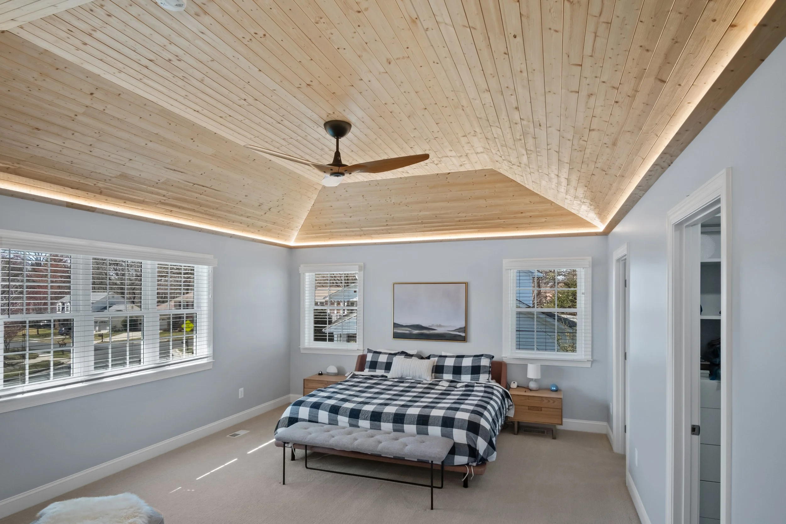 Finished bedroom with a vaulted wood ceiling, perimeter lighting and windows.