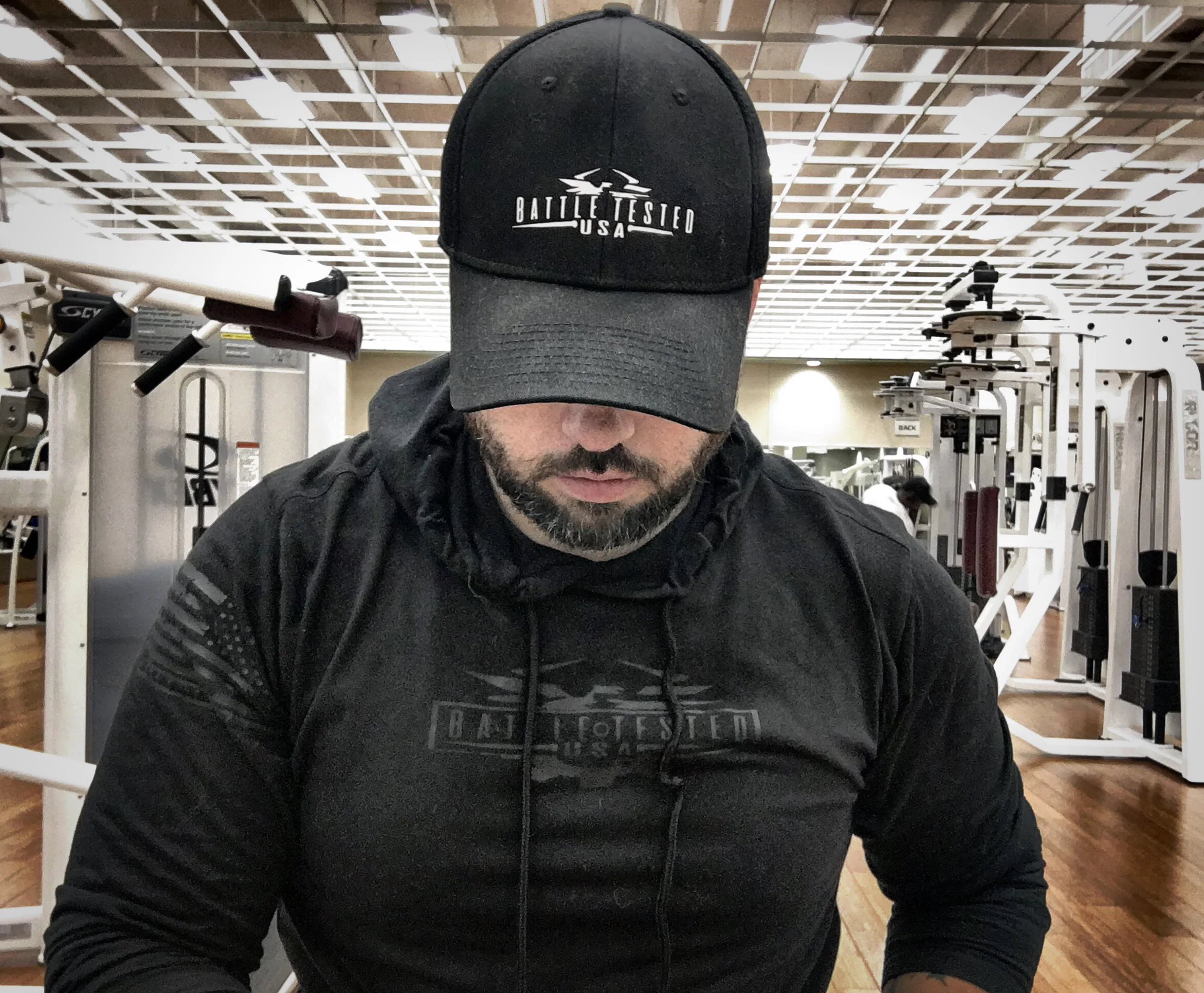 A man in a gym wearing an original Battle Tested USA cap and hoodie