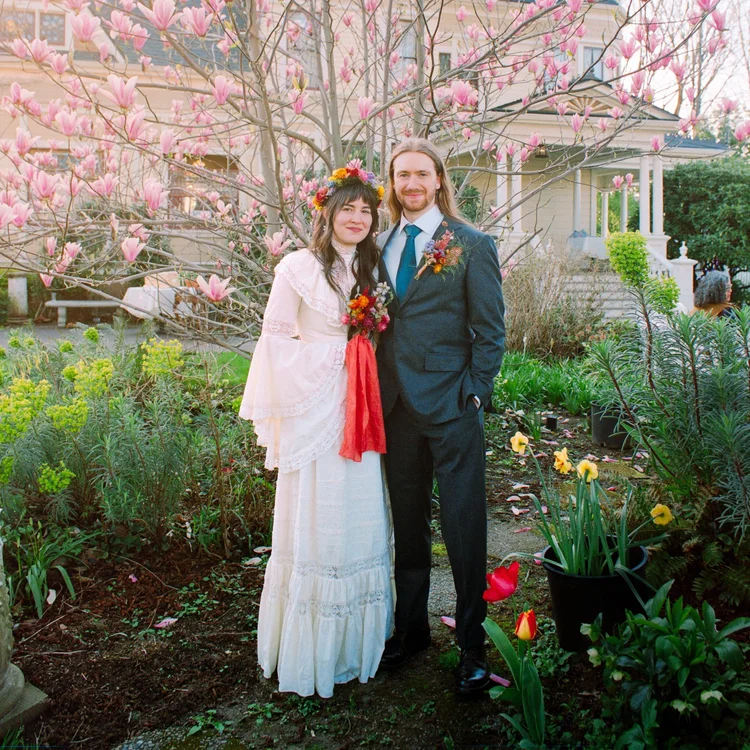 A couple stands under a flowering tree at their wedding.