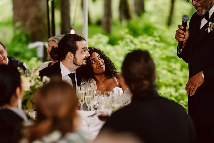 A bride and a groom listen to a toast on their wedding day.
