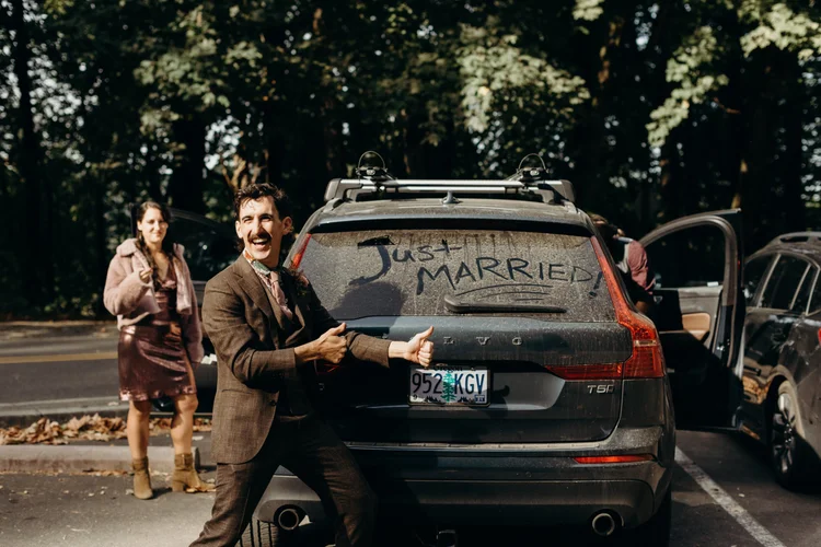 A groom celebrates by his dirty car on his wedding day.
