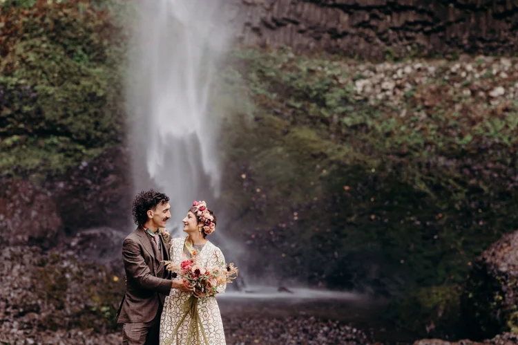 A bride and a groom on their wedding day, in front of a waterfall.