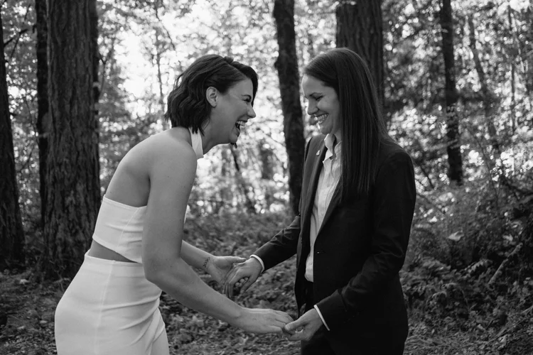 Two brides smile and hold hands on their wedding day.