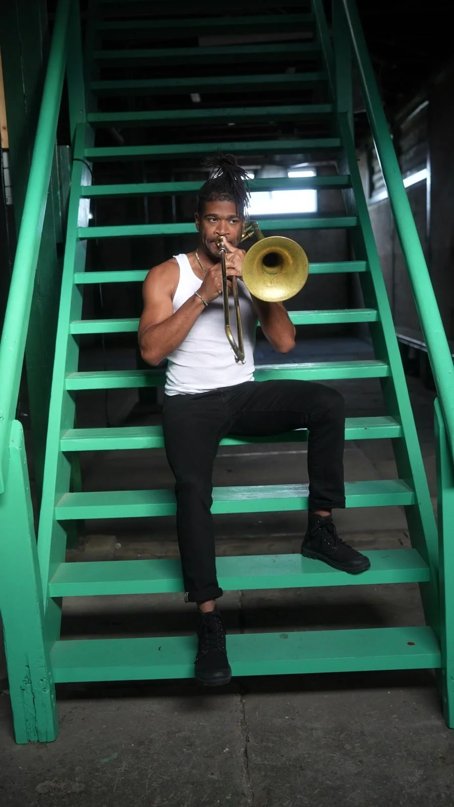 Darius Christian playing trombone on green stairs in Amsterdam