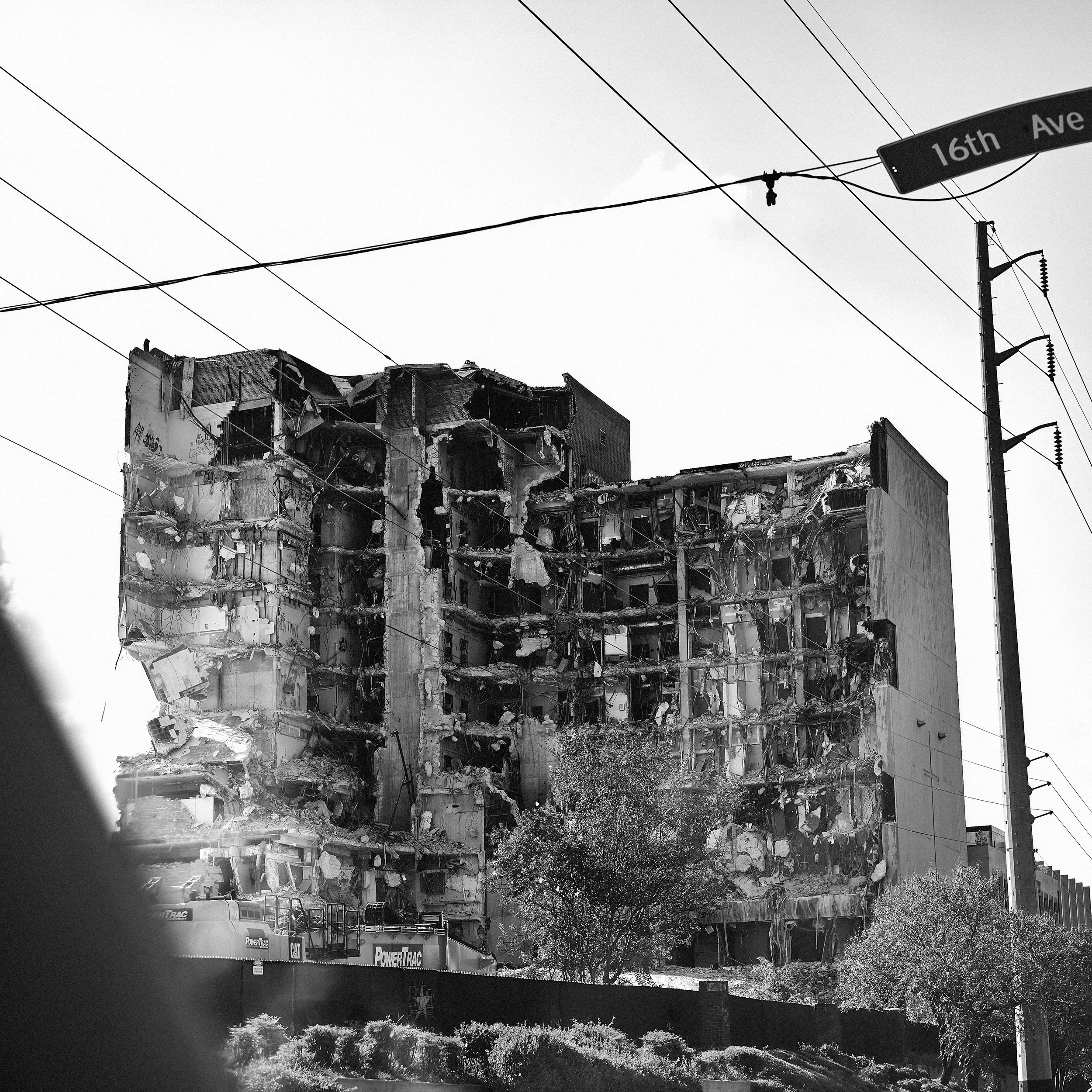 Partially demolished building beneath a 16th Avenue street sign, with equipment and fencing below