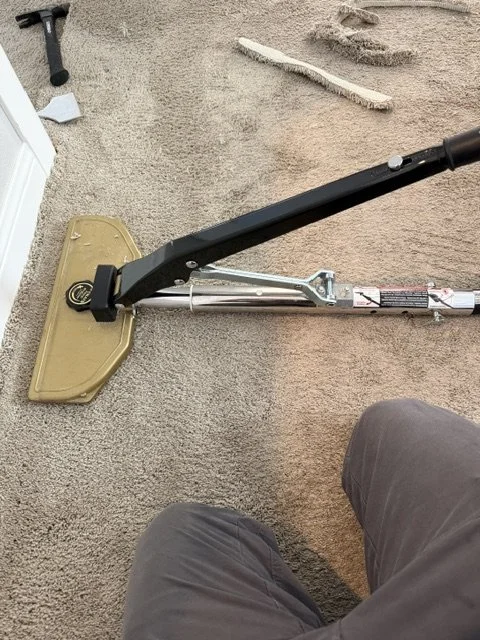 Power stretcher set up on carpet over a wood subfloor, with trimmed carpet strips nearby