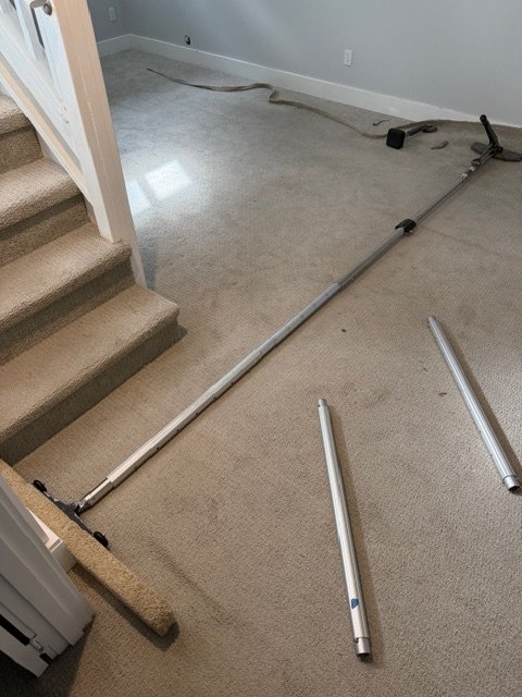 Power stretcher poles set up on a concrete floor before stretching carpet in a basement