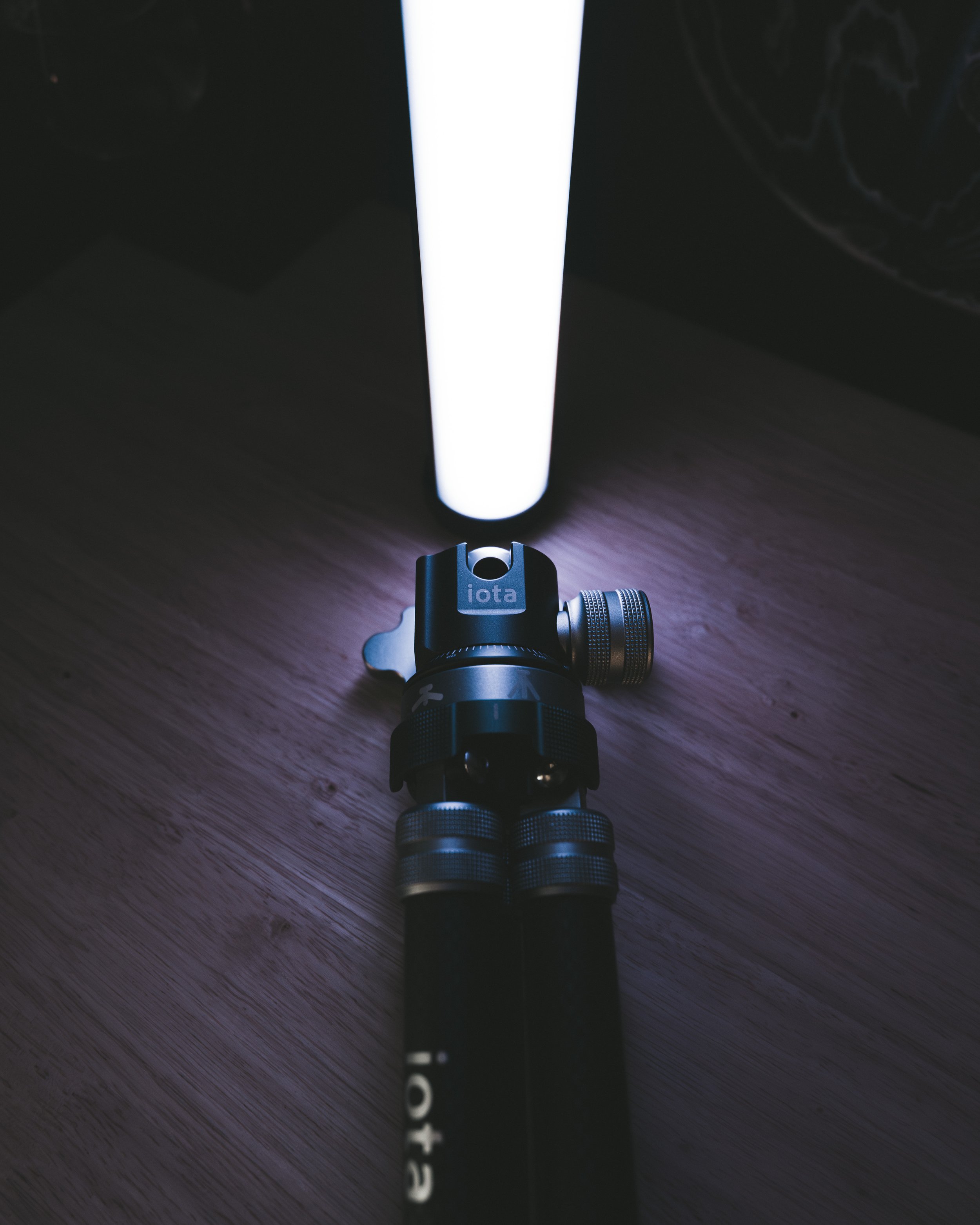 ProMaster iota 219 tripod holding an RGB tube light on a dark wood surface