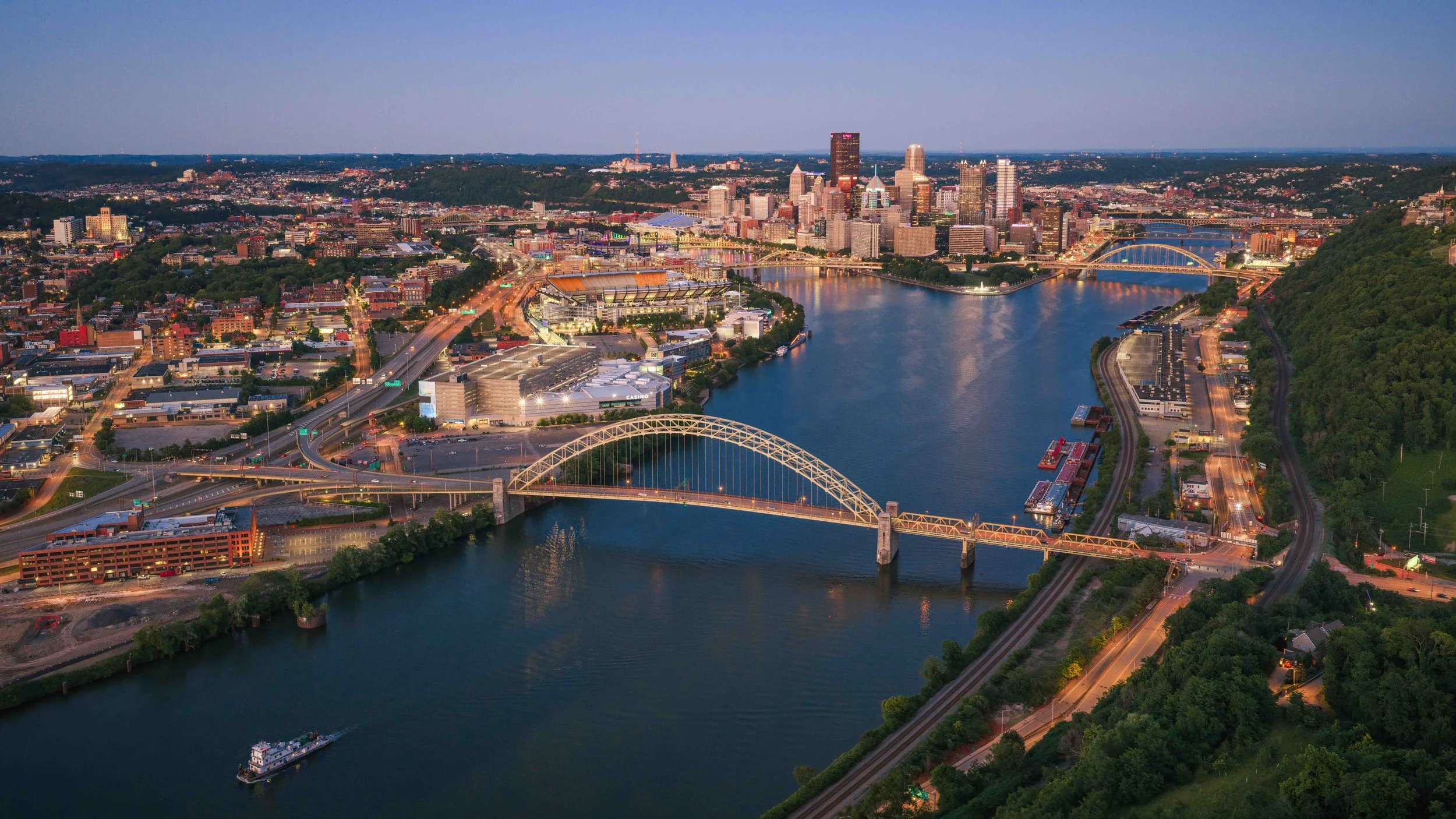 Aerial drone photo of downtown Pittsburgh at blue hour, showing the skyline, riverfront, bridges, stadiums, and city lights for professional drone photography and videography by Ian Jones of ISJDESIGNS.