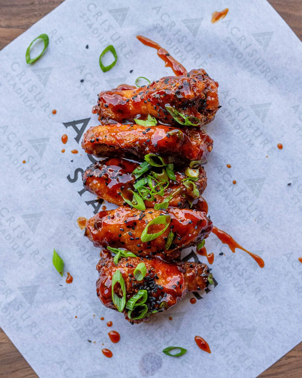 Double fried Korean wings with gochujang glaze, sesame, and scallion on Acrisure Stadium paper, Pittsburgh food photography for Aramark by Ian Jones