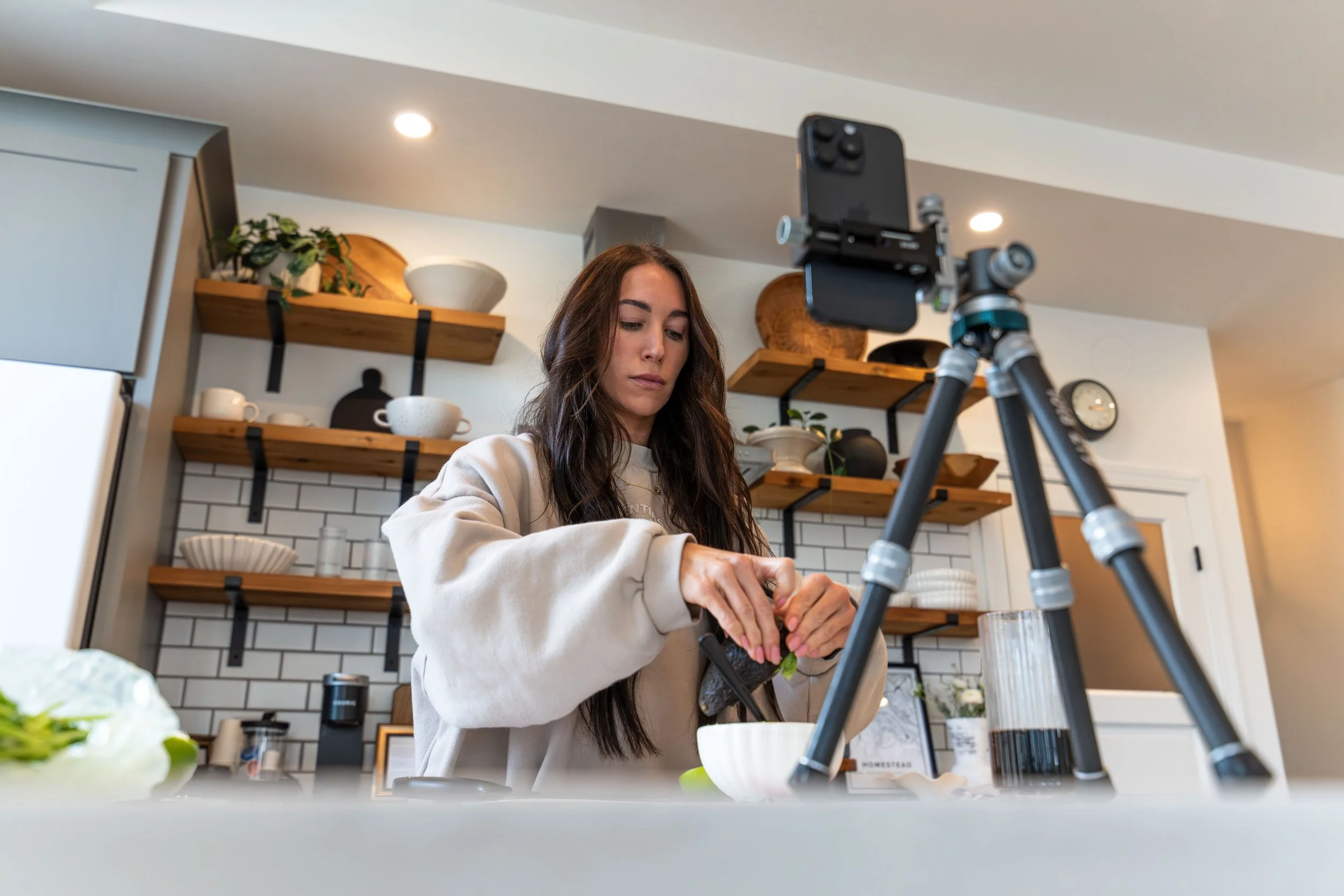 Behind-the-scenes kitchen content shoot by Ian Jones of ISJDESIGNS showing a creator preparing food while filming with a phone tripod, photographed with the Tamron 35-100mm.