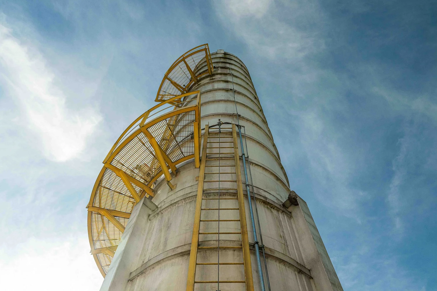 Low-angle industrial facility photography of a tall cryogenic storage silo with a yellow caged ladder and maintenance platforms, showing the scale of plant infrastructure and equipment.