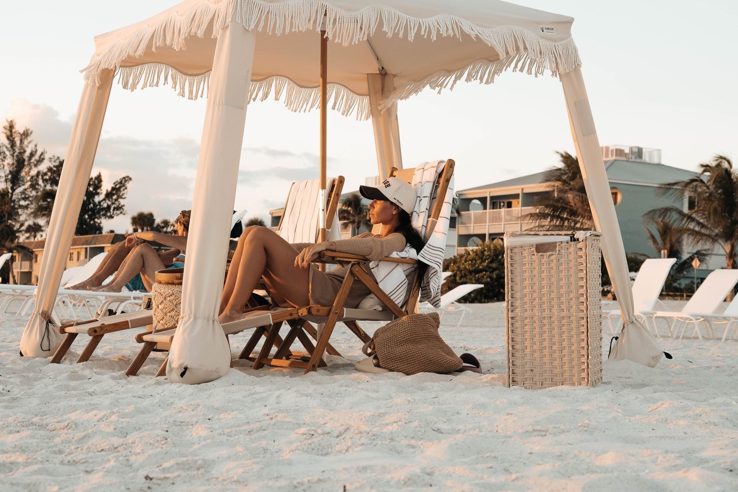 Guests relaxing under a fringed beachfront cabana at golden hour in Florida, hotel and resort lifestyle photography for hospitality marketing.