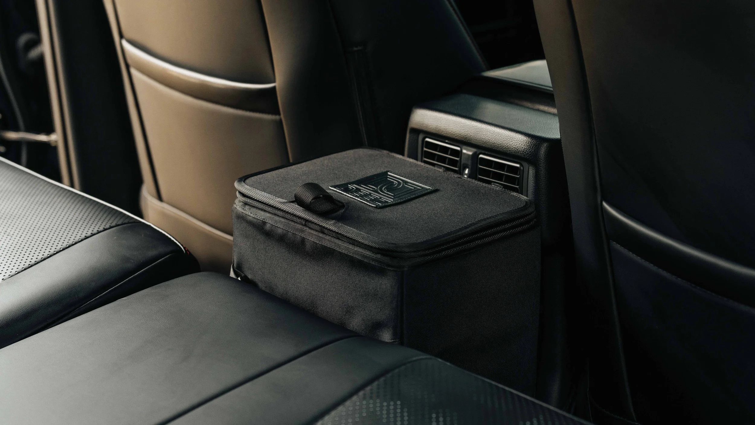 Black Double Deez Goodz trash can positioned behind the front seats of an SUV, lifestyle product photography by Ian Jones of ISJDESIGNS.