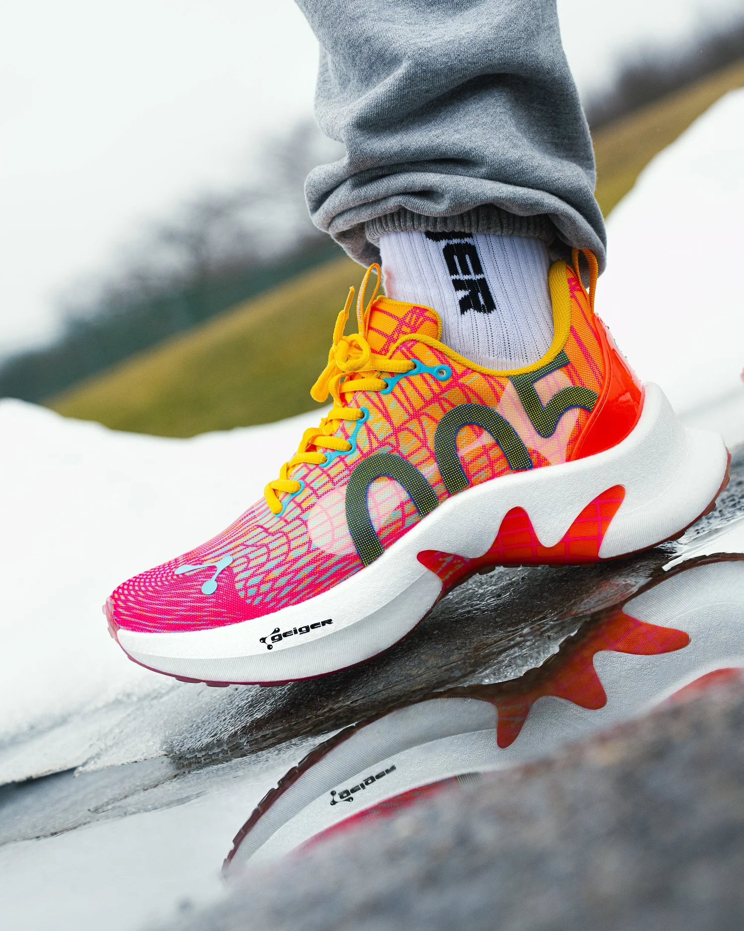 Lifestyle product photography by Pittsburgh photographer Ian Jones for ISJDESIGNS, showing a John Geiger 005 Orange Burst sneaker on foot with reflection detail and commercial campaign styling.
