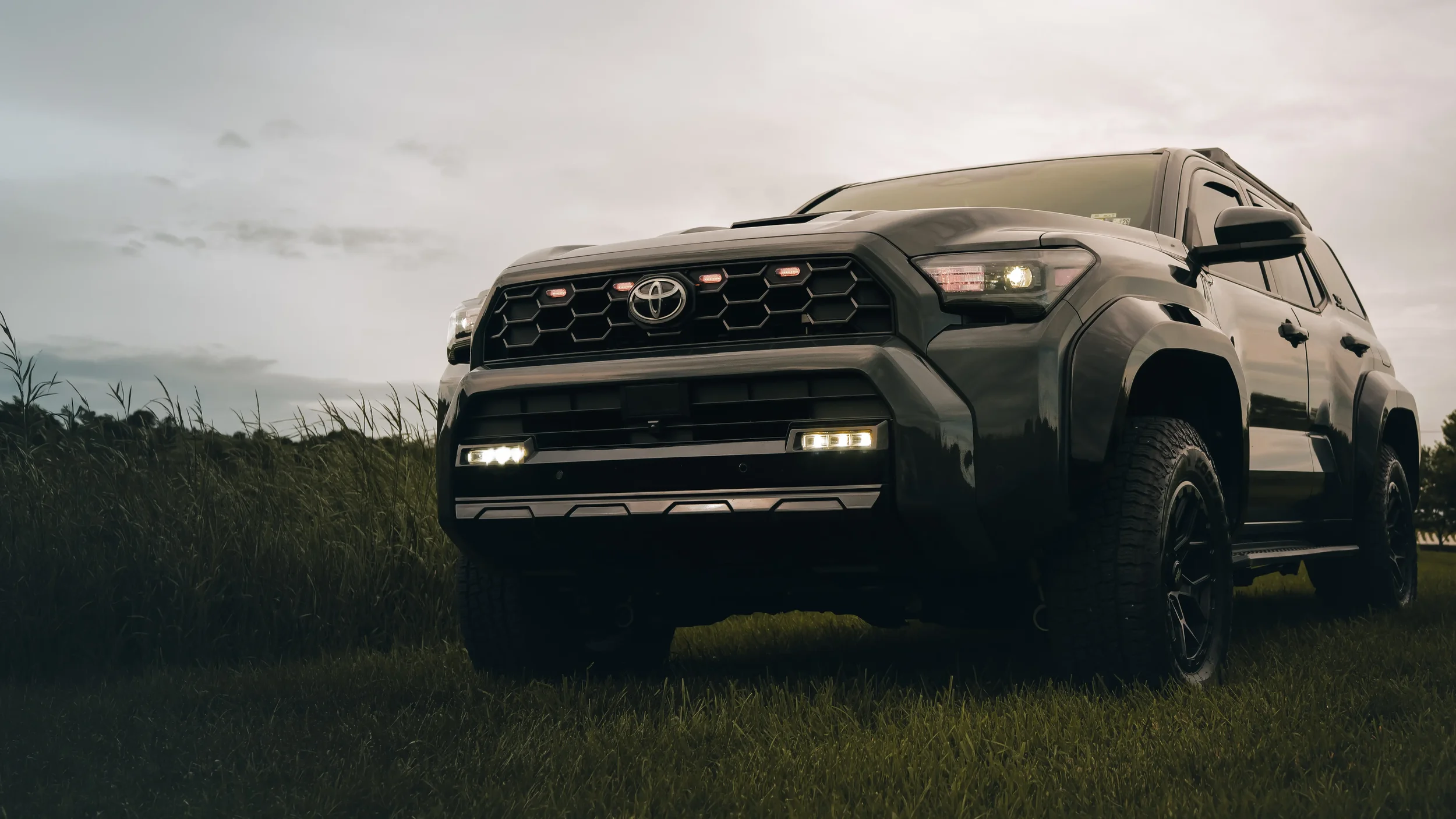 Rough Country M1R Reservoir Loaded Struts installed on Ian Jones' 2025 Toyota 4Runner TRD Sport, front-end leveled stance with raptor grille lights and gloss black wide fender flares.