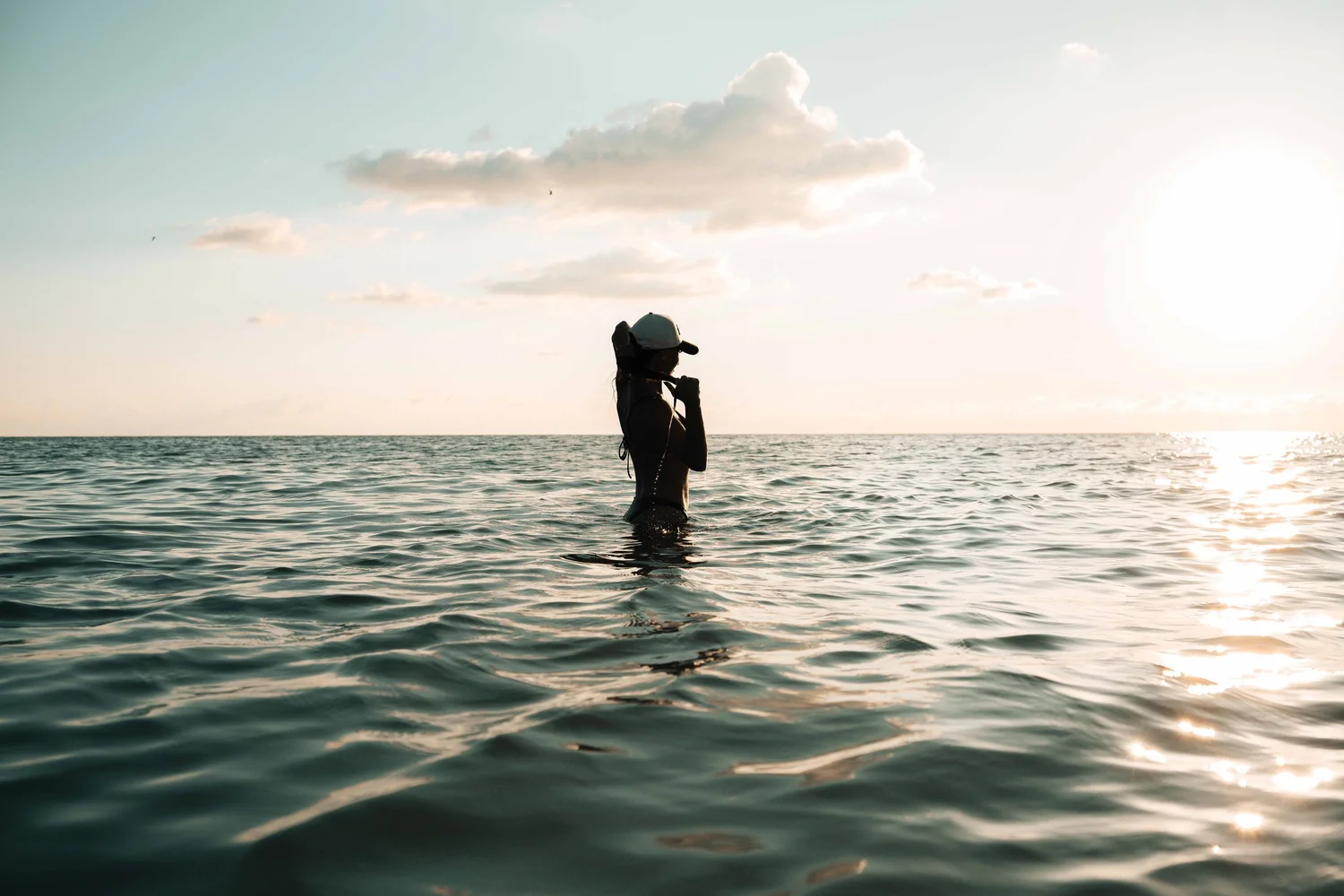 Woman silhouetted in calm Gulf water at sunset on Anna Maria Island, Florida, on-location hospitality lifestyle photography for resort and destination marketing.