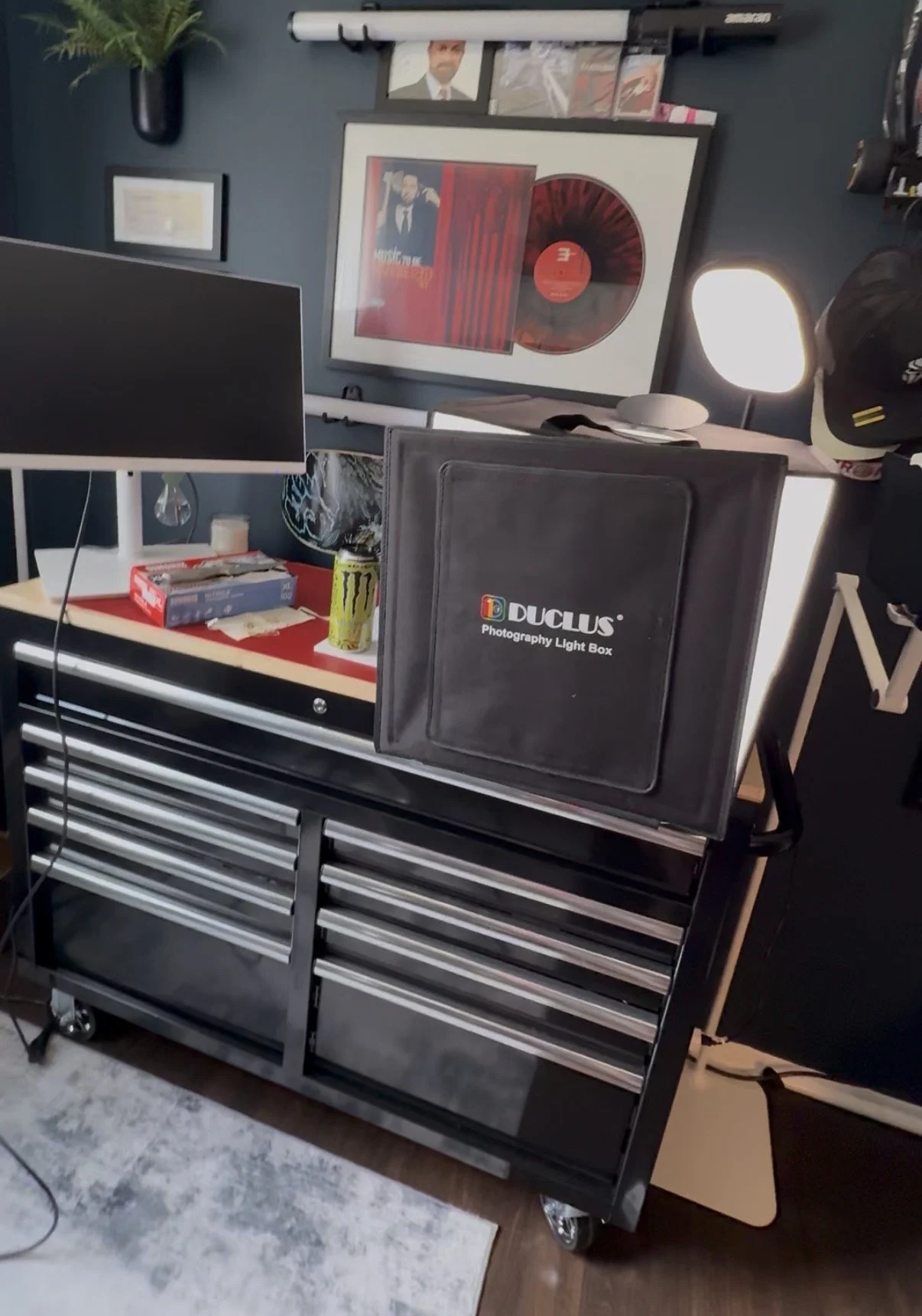 DUCLUS 16-inch portable photography lightbox, assembled with its front cover closed, sitting on a black rolling tool chest in Ian Jones's product photography workspace beside a monitor and an LED light