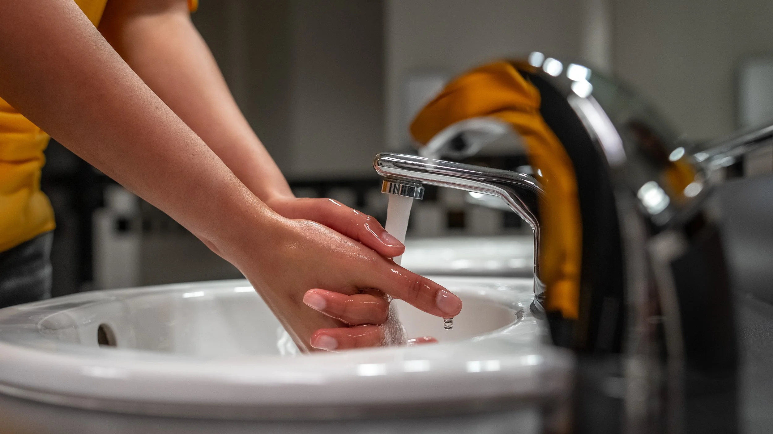 Hands being washed under a touchless chrome faucet at an Acrisure Stadium restroom sink, commercial facility photography by Pittsburgh photographer Ian Jones for a Kimberly-Clark Professional project.