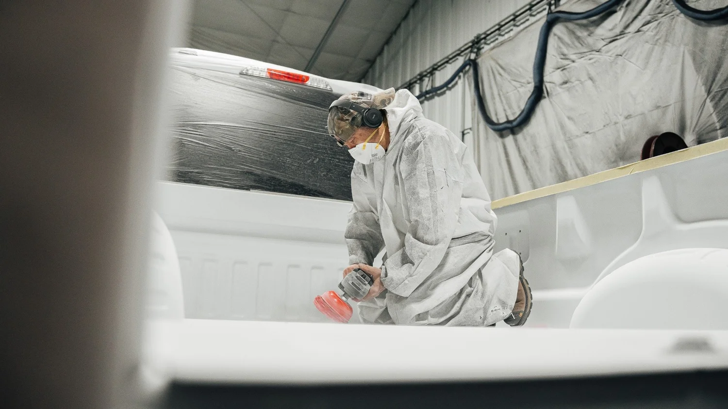 Automotive paint booth photography by Pittsburgh commercial industrial photographer Ian Jones for ISJDESIGNS, showing a technician refinishing a truck bed in a protective suit inside a commercial shop.