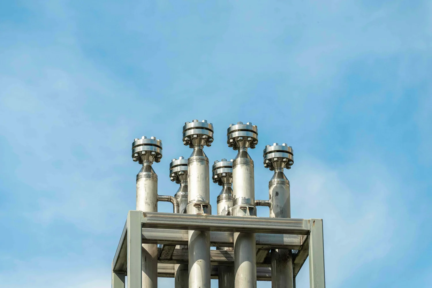 Industrial photography of stainless steel pressure vessels and bolted flange heads against a blue sky, showcasing engineered process equipment and manufacturing infrastructure.