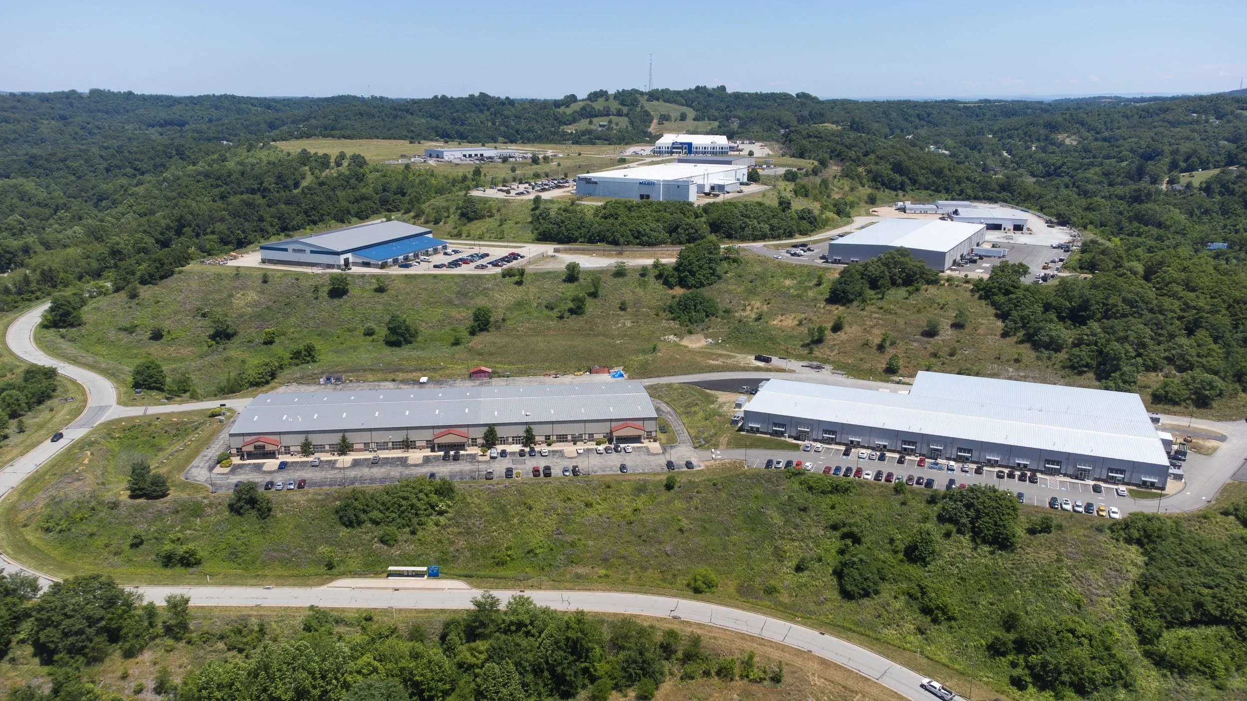 Aerial drone photo of a commercial business park near Pittsburgh with industrial buildings, roads, parking areas, and surrounding land development.
