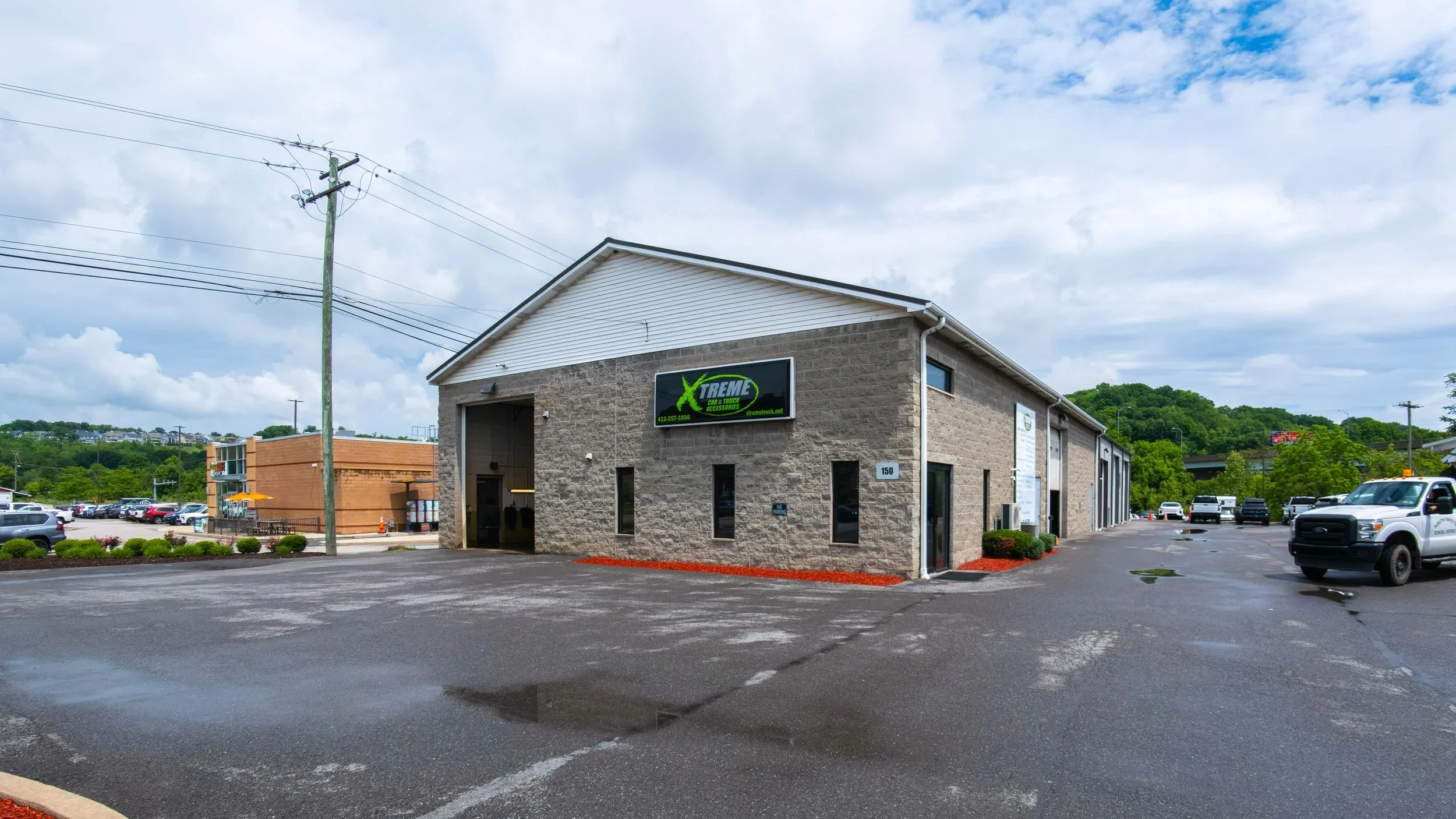 Exterior of Xtreme Car and Truck Accessories in Bridgeville, Pennsylvania, photographed from the parking lot approach with the sign, phone number and open service bay all clearly visible