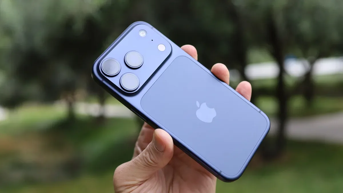 iPhone 18 Pro held at an angle outdoors, showing the raised rear camera plateau with the 48MP Fusion Main, 48MP Fusion Ultra Wide, and 100mm tetraprism Telephoto lenses arranged in a triangle.