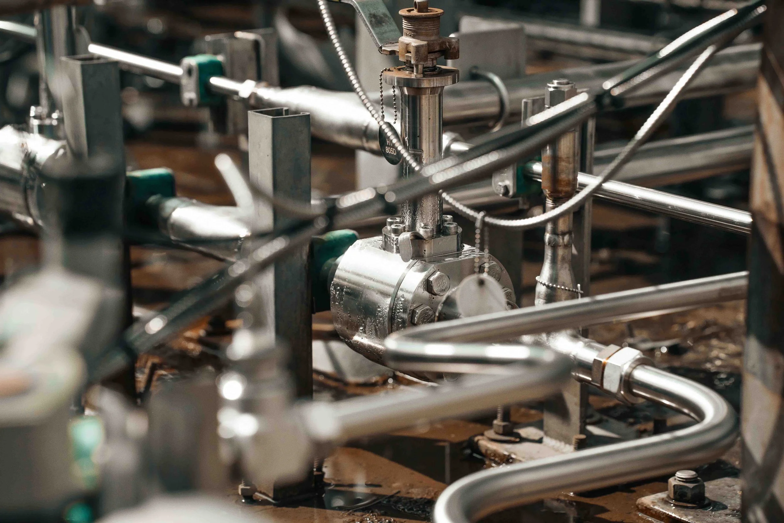 Detailed industrial photography of a stainless steel control valve, instrumentation tubing and process piping, highlighting precision engineering and complex facility equipment.
