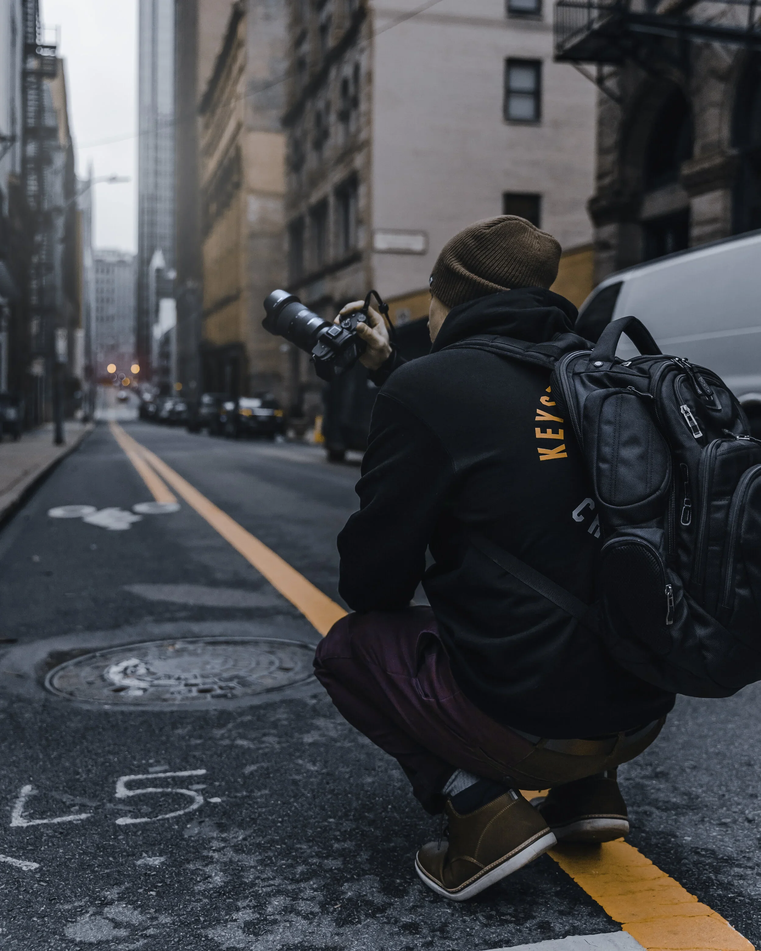 Ian Jones crouched on a downtown Pittsburgh street shooting with a Sony a1 and Tamron zoom, camera bag on his back, working the same way he photographs businesses for Google Business Profiles