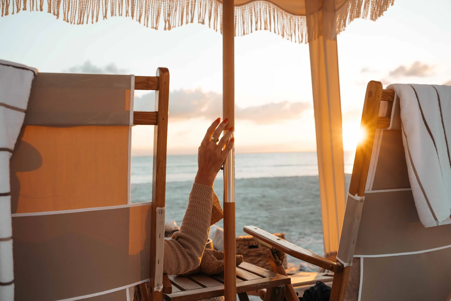 Guest relaxing between wooden beach chairs under a cabana at sunset, candid hotel and resort photography showing the hospitality guest experience.