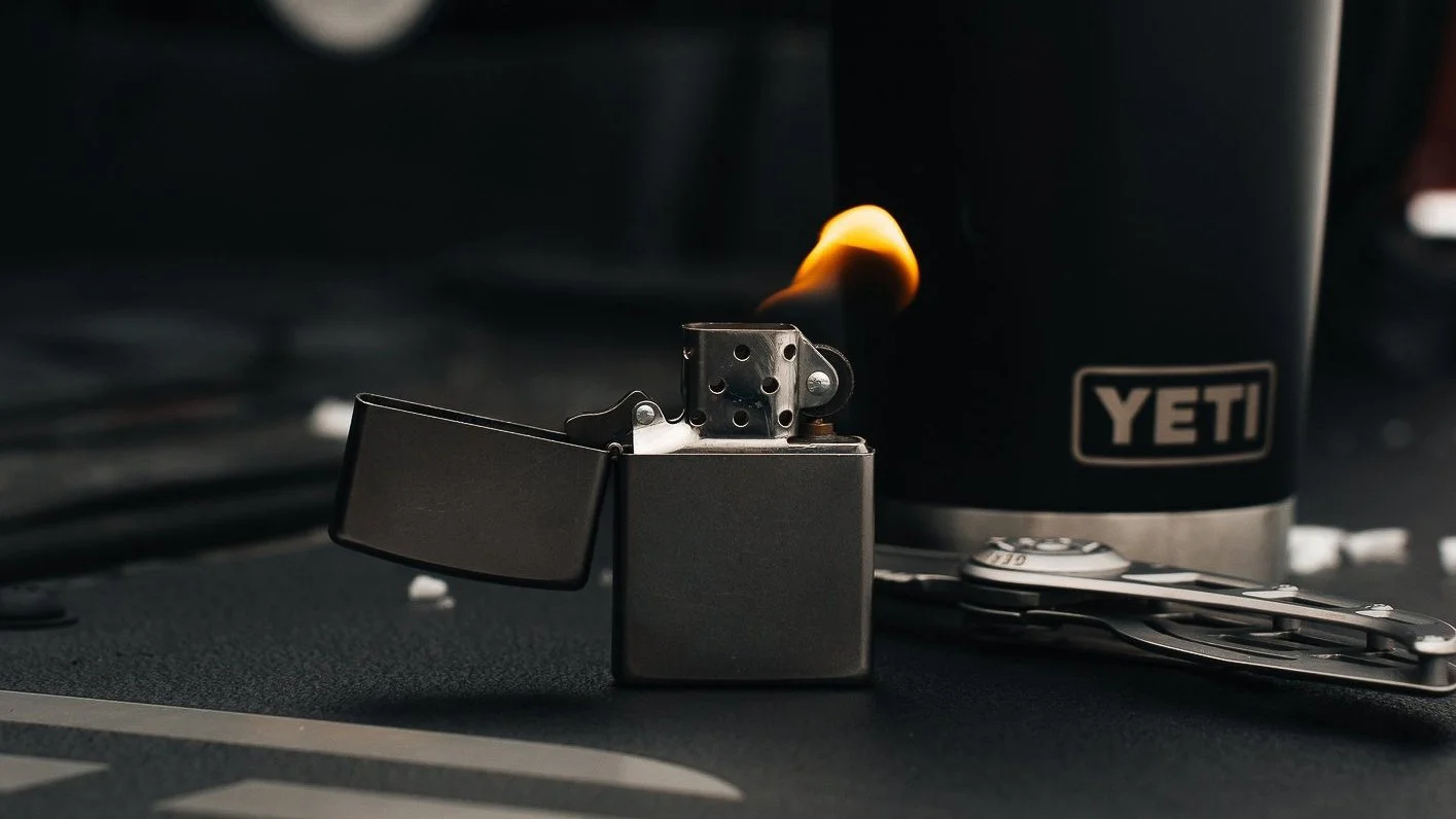 Commercial product photography in Pittsburgh by Ian Jones of ISJDesigns featuring a lit Zippo lighter beside a YETI cup and pocket knife.