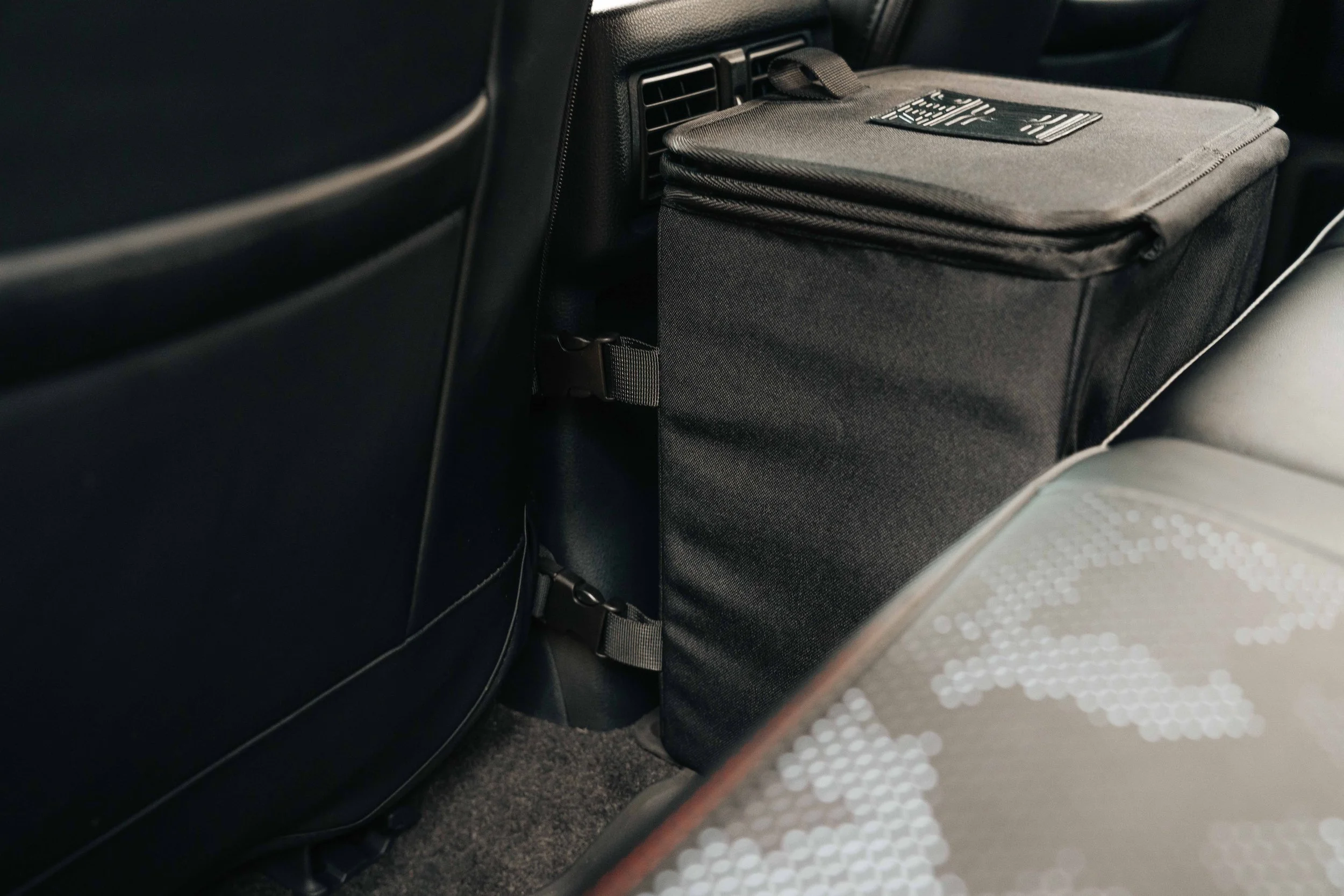 Double Deez Goodz vehicle trash can secured behind a front seat with mounting straps visible, product photography by Ian Jones of ISJDESIGNS.