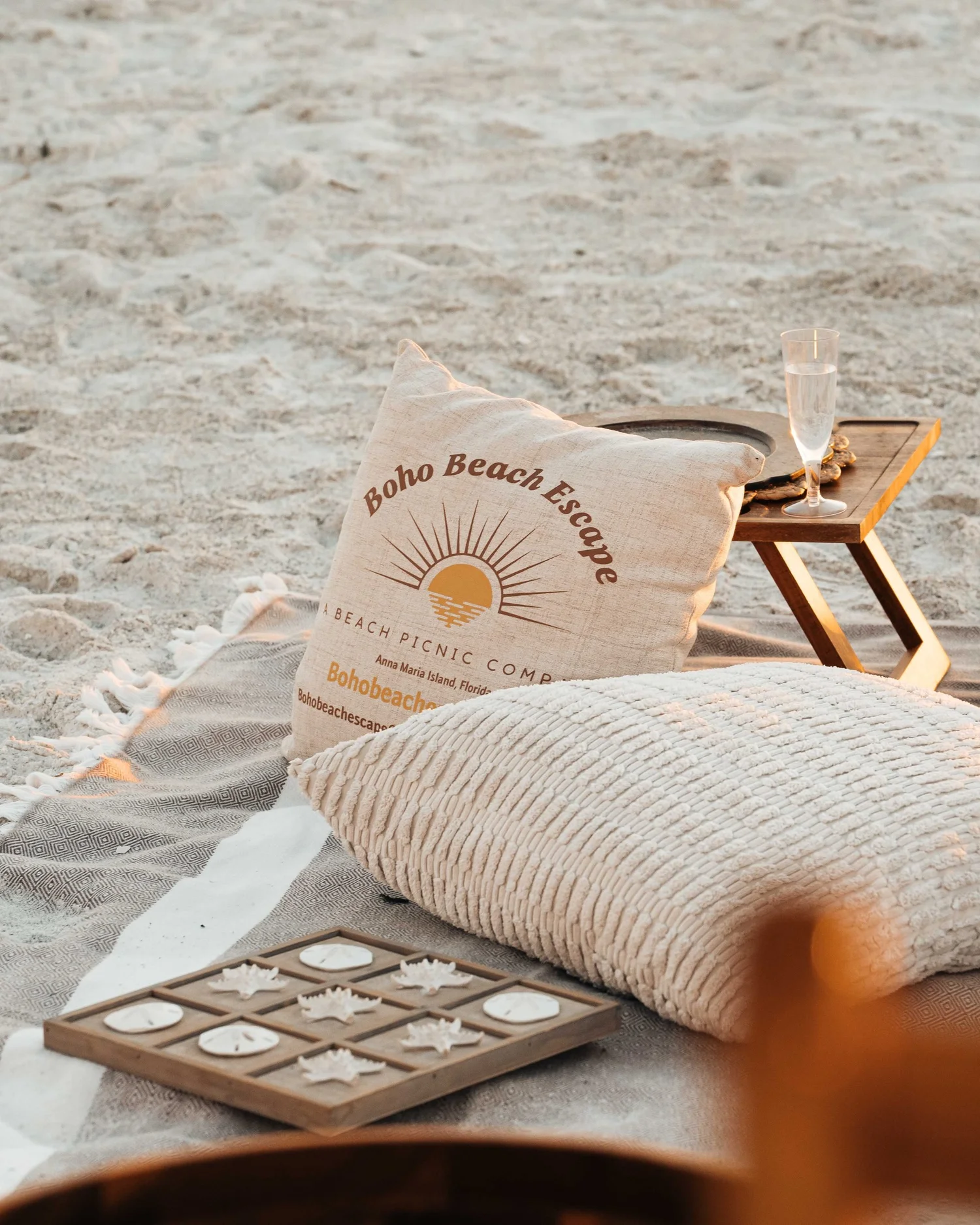 Sun logo pillow, cushion, and shell game detail at a beach picnic, vertical hospitality content for hotel, resort, and experience brand social media.