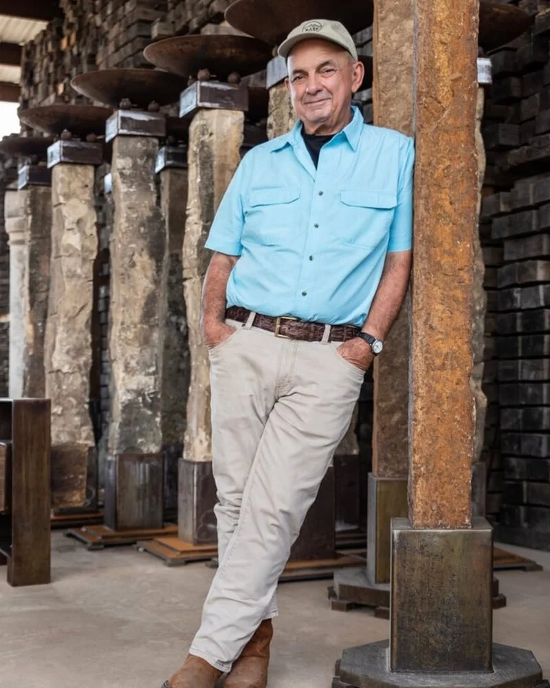 Paul Michael leaning against a stone and steel column in his Dermott workshop