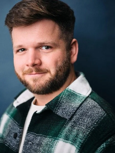 Dennis Connors headshot, theatrical: sideways glance, green flannel, blue backdrop.
