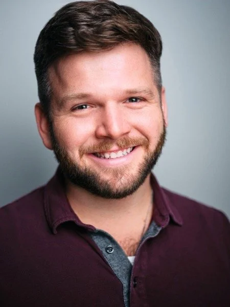 Dennis Connors headshot, commercial: big open smile, burgundy shirt, grey backdrop.