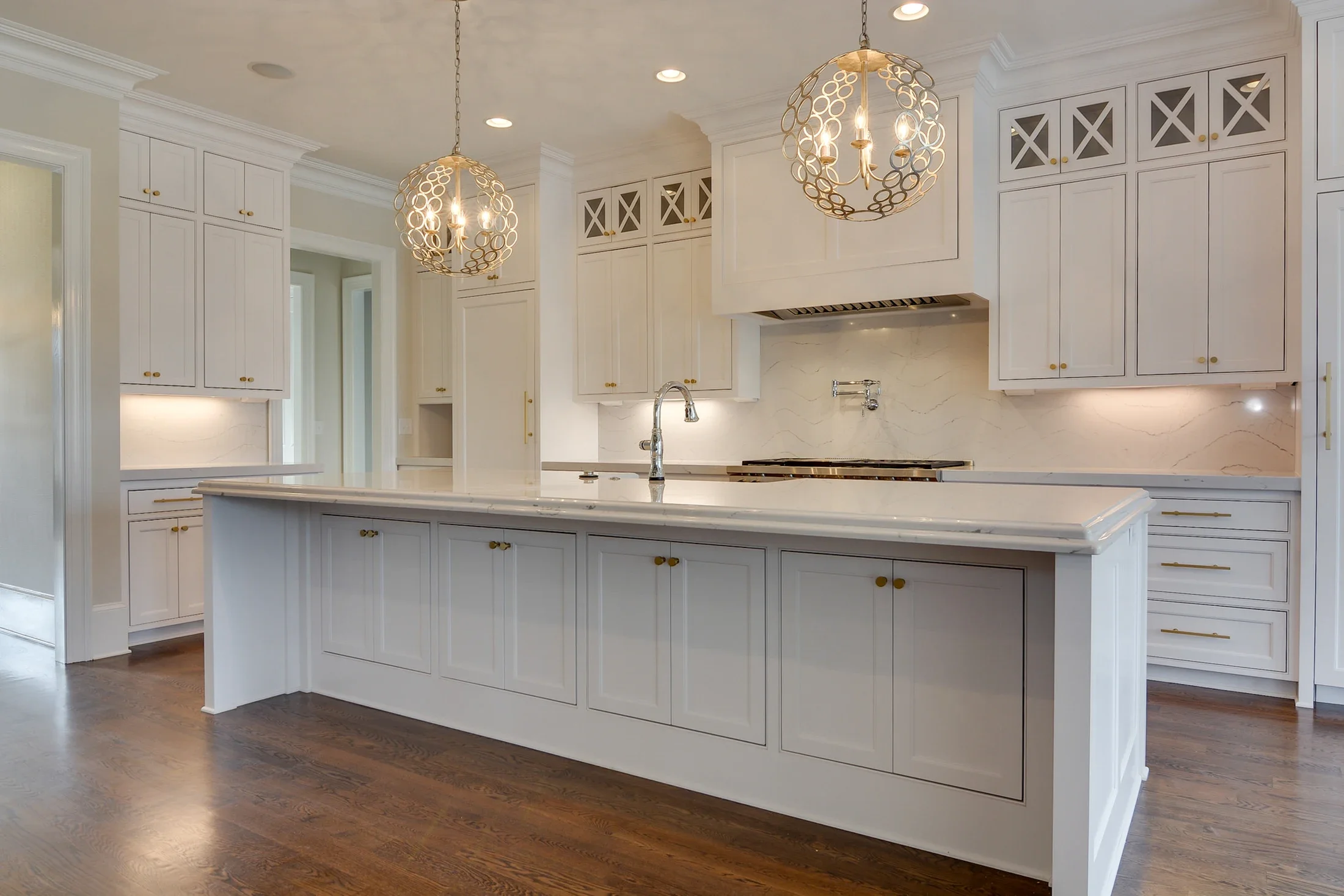An elegant white kitchen with a large island and decorative pendant lights