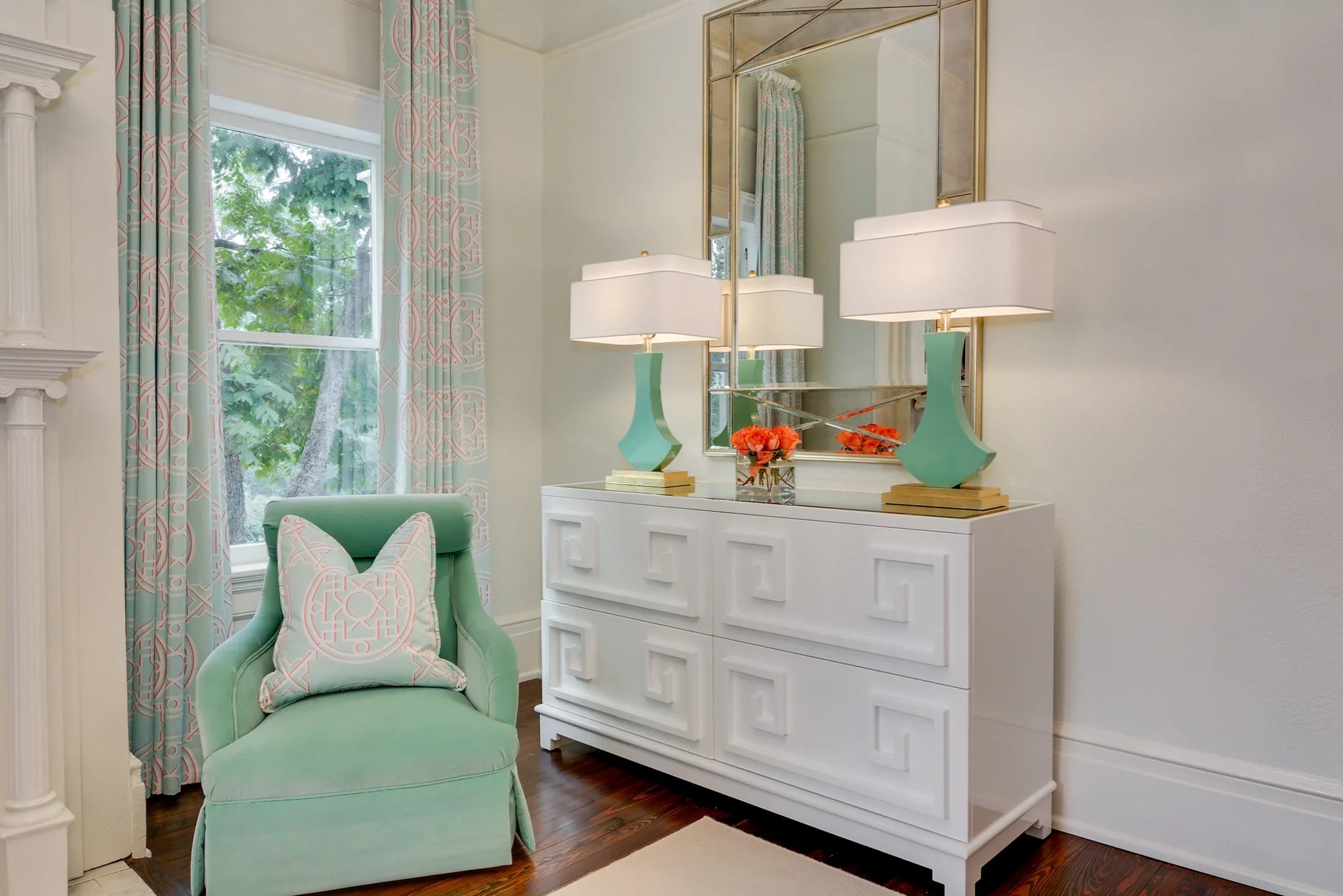 A mint-green accent chair beside a white dresser and a large sunlit window