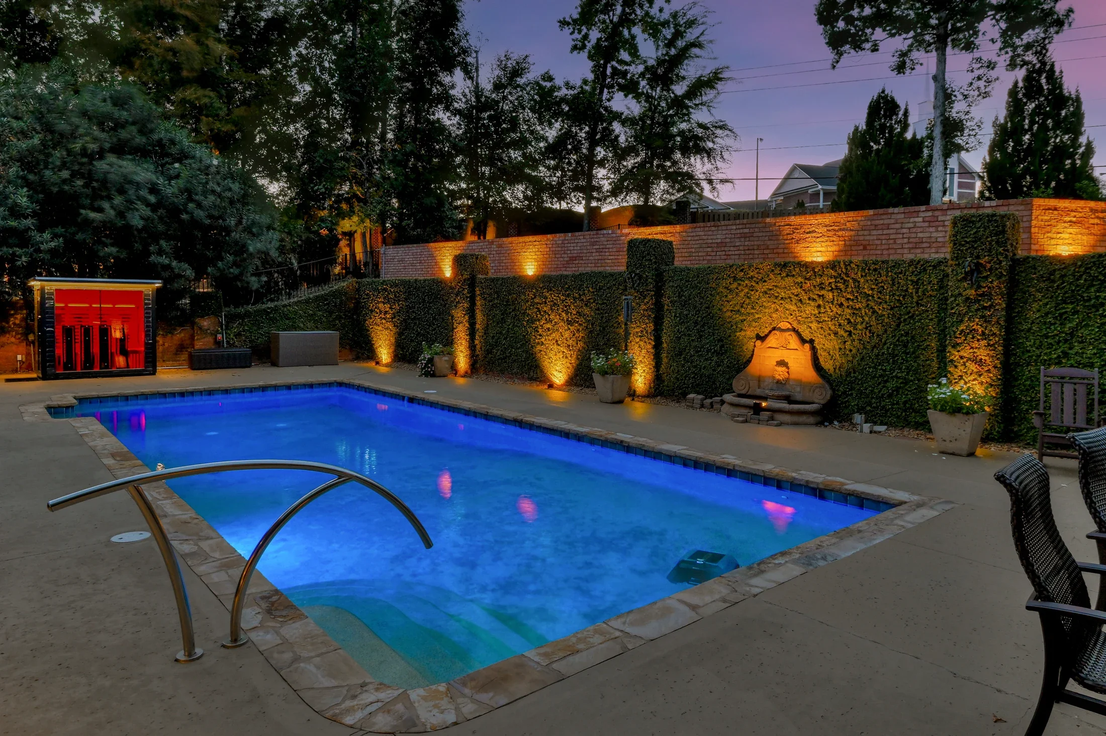 A blue-lit swimming pool and landscaped courtyard at dusk