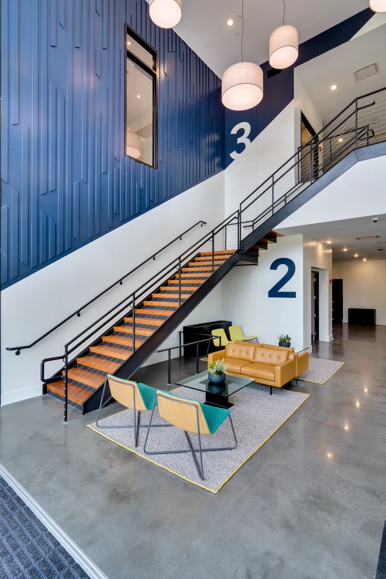 A modern multilevel interior with a blue feature wall, open staircase, and pendant lighting