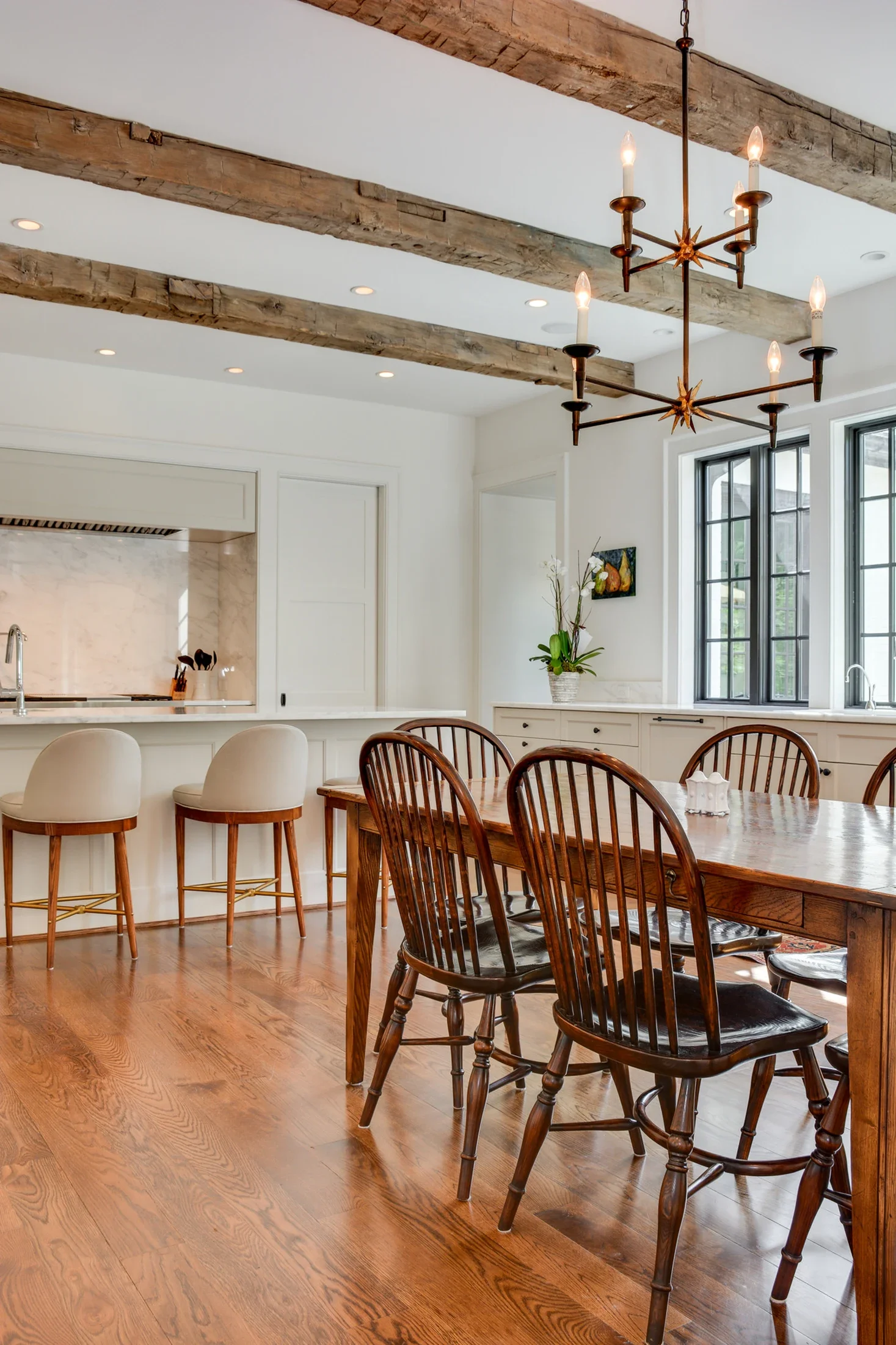 Dining room with exposed wooden ceiling beams opening into a bright kitchen