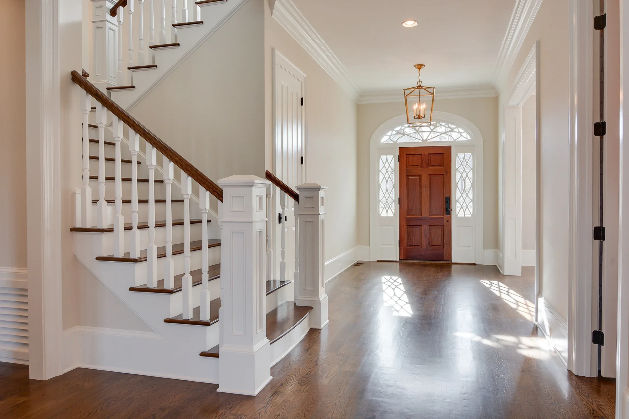 A bright entrance hall with a white staircase and warm wooden front door